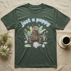 Asian Water Monitor Baby T-Shirt in Military Green — Asian water monitor with tongue out among pastel reeds and lotus under puffy blue bubble text "just a puppy".