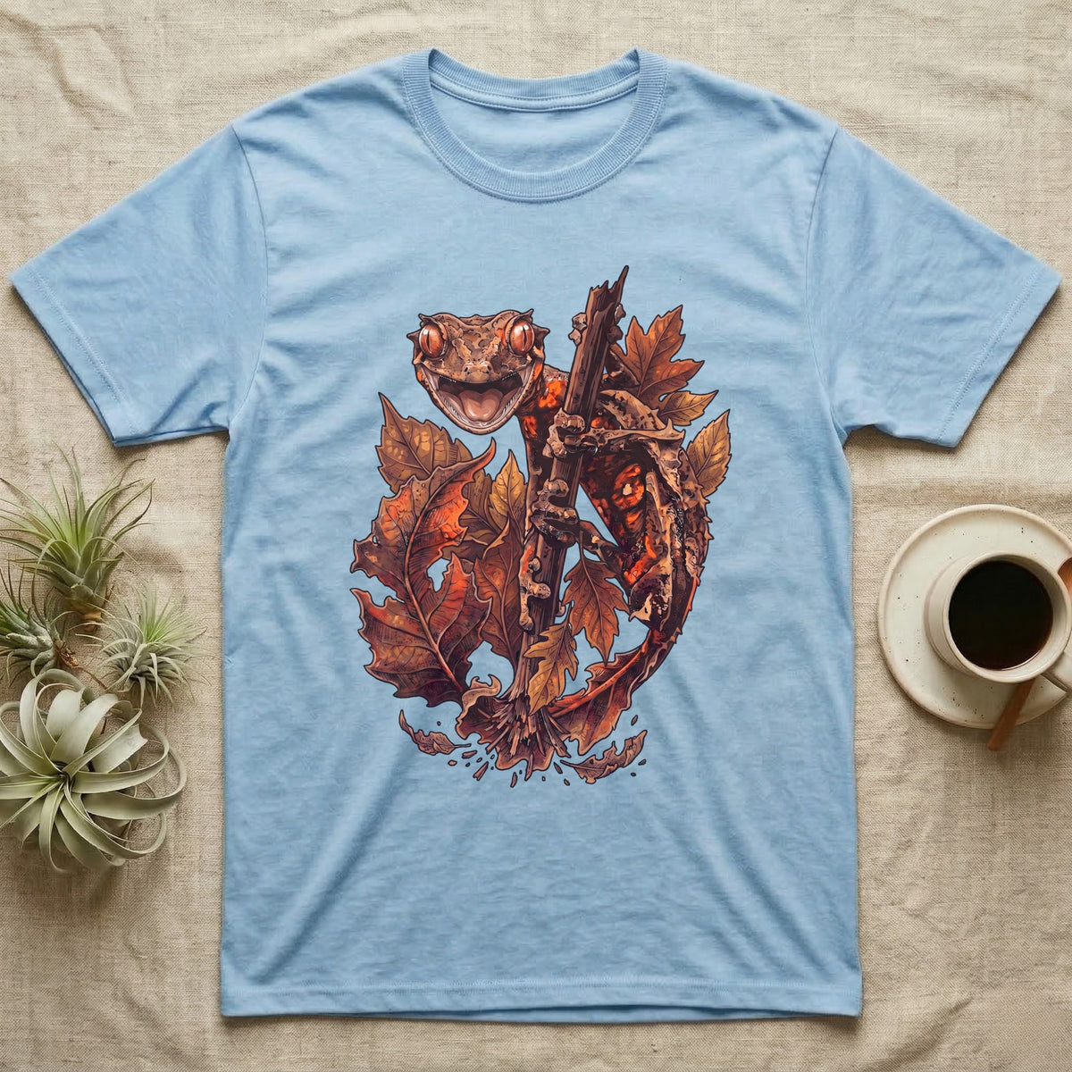 Satanic Leaf-Tailed Gecko Autumn T-Shirt in Light Blue — Painted illustration of a satanic leaf-tailed gecko gripping a bare stem among dried autumn leaves in rust and amber, no on-shirt text.