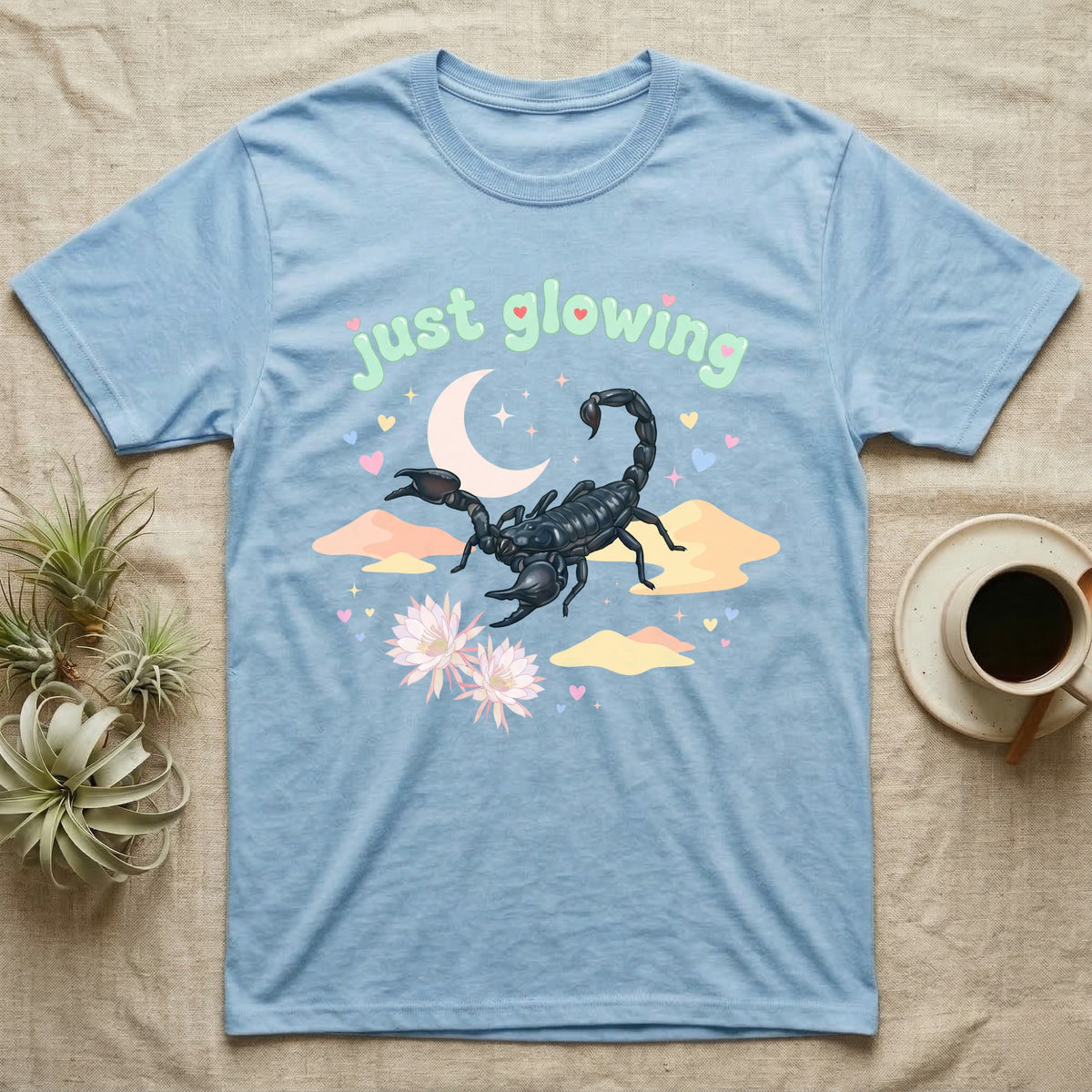 Emperor Scorpion Baby T-Shirt in Light Blue — Black emperor scorpion, pincers raised, under a pastel moon and stars with puffy mint bubble text "just glowing".