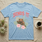 Crested Gecko Feral T-Shirt in Light Blue — Crested gecko on a mossy branch in a pastel jungle scene under a spiky coral metal wordmark reading SENDS IT.