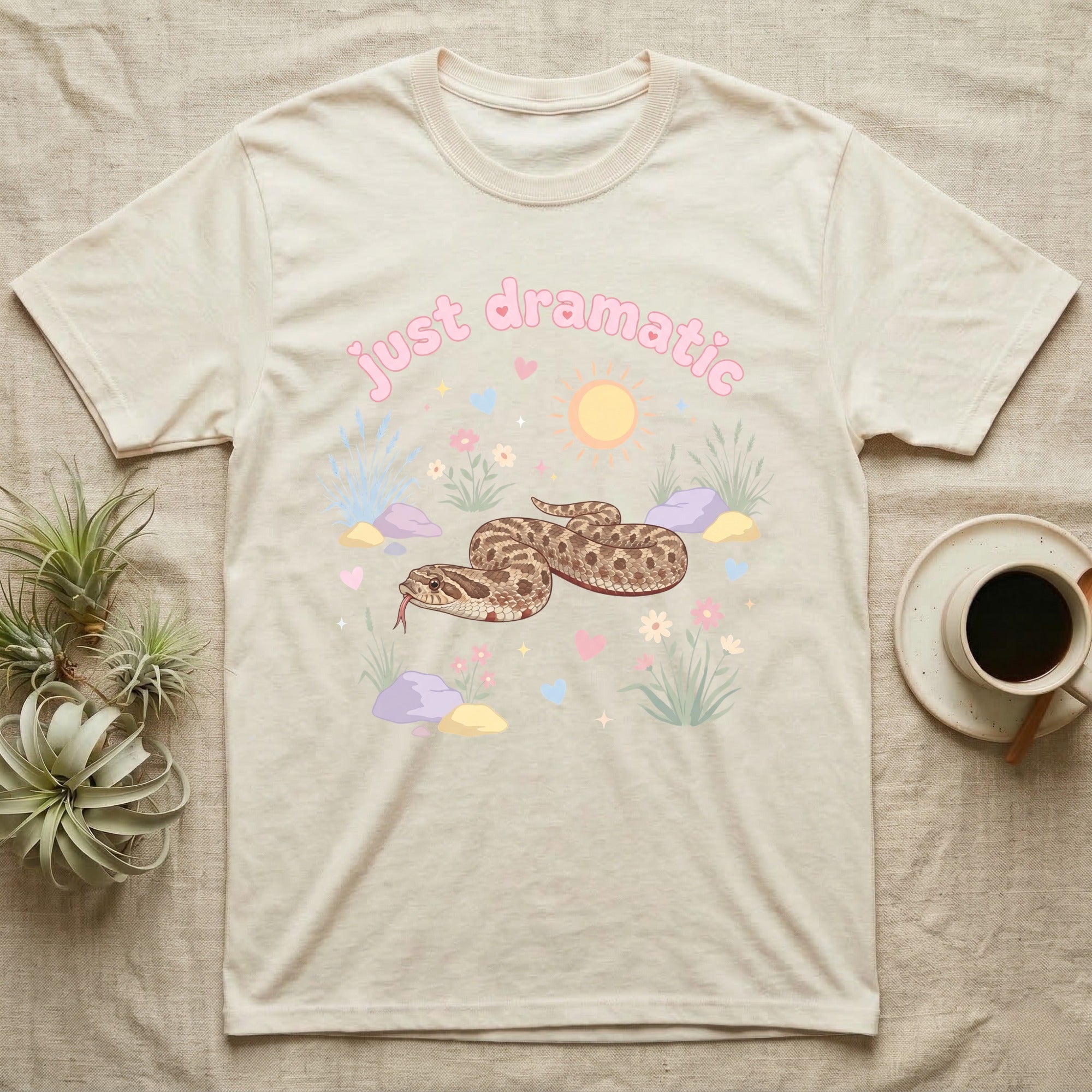Western Hognose Snake Baby T-Shirt in Natural — Pastel western hognose snake in a low coil with tongue out among grasses, puffy pink bubble wordmark "just dramatic" above.