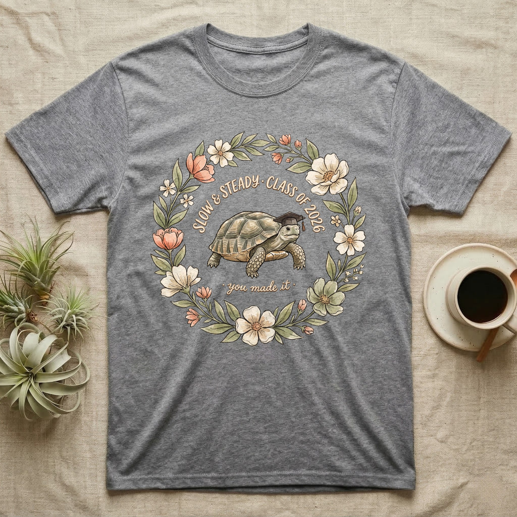 Slow And Steady Graduation T-Shirt in Sport Grey — Watercolour illustration of a tortoise in a graduation cap inside a floral wreath with "Slow & Steady, Class of 2026."