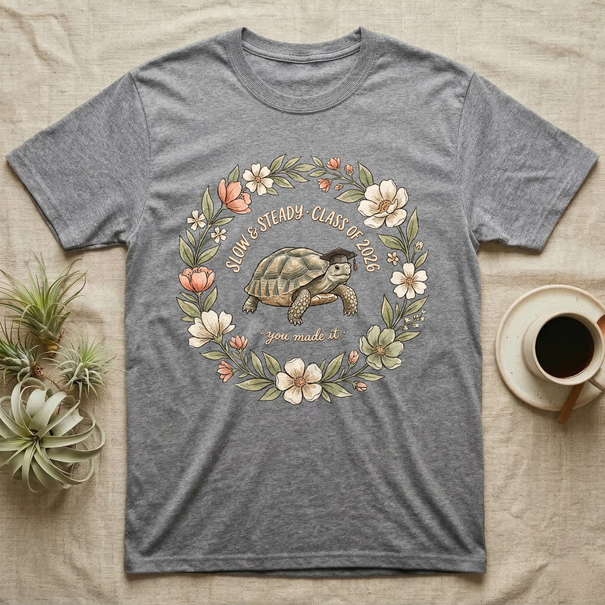 Slow And Steady Graduation T-Shirt in Sport Grey — Watercolour illustration of a tortoise in a graduation cap inside a floral wreath with "Slow & Steady, Class of 2026."
