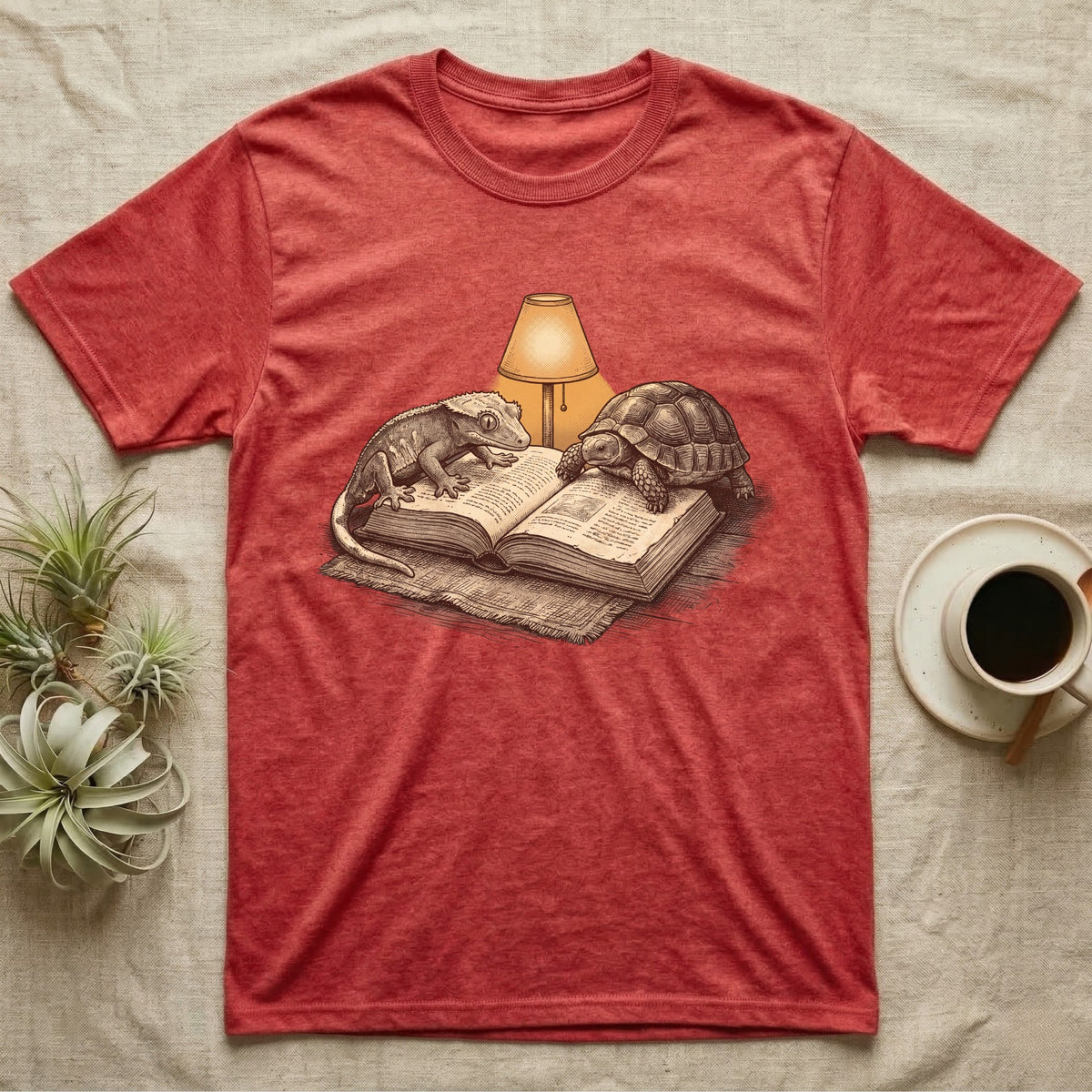 Cold-Blooded Book Club T-Shirt in Heather Red — Engraved cozy illustration of a gecko and a tortoise sharing an open book under a glowing reading lamp.