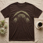 Snapping Turtle Stare T-Shirt in Dark Chocolate — Single-ink common snapping turtle seen head-on under its shell, lit from above, staring at the viewer on black.