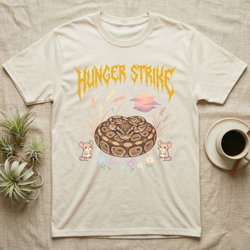 Ball Python Feral T-Shirt in Natural — Ball python coiled in a loaf in a pastel savanna scene under a spiky honey-gold metal wordmark reading HUNGER STRIKE.
