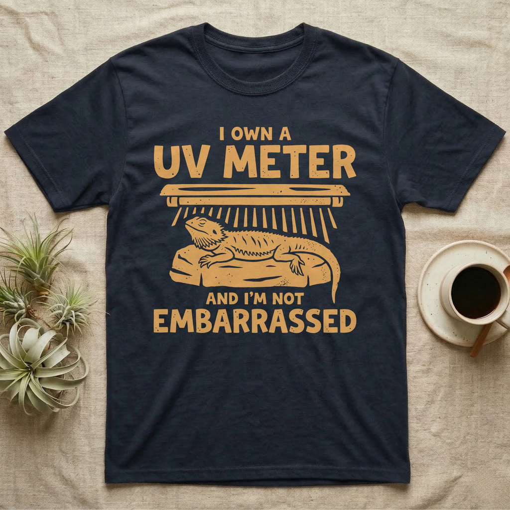 Reptile Keeper UV Meter T-Shirt in Navy — Linocut block-print badge of a UVB tube lamp above an empty basking rock, ringed by carved slogan lettering.