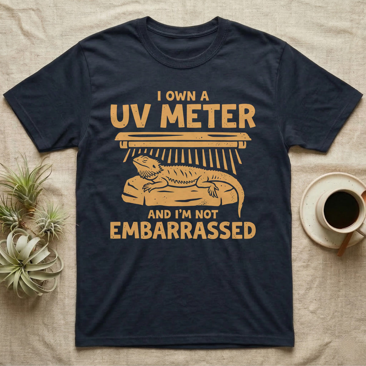 Reptile Keeper UV Meter T-Shirt in Navy — Linocut block-print badge of a UVB tube lamp above an empty basking rock, ringed by carved slogan lettering.