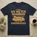 Reptile Keeper UV Meter T-Shirt in Navy — Linocut block-print badge of a UVB tube lamp above an empty basking rock, ringed by carved slogan lettering.