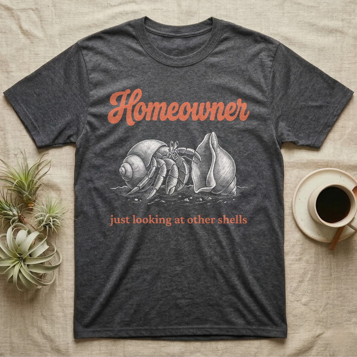 Hermit Crab Homeowner T-Shirt in Dark Heather — White-line engraving of a land hermit crab eyeing a bigger empty shell, under orange script Homeowner and a serif line