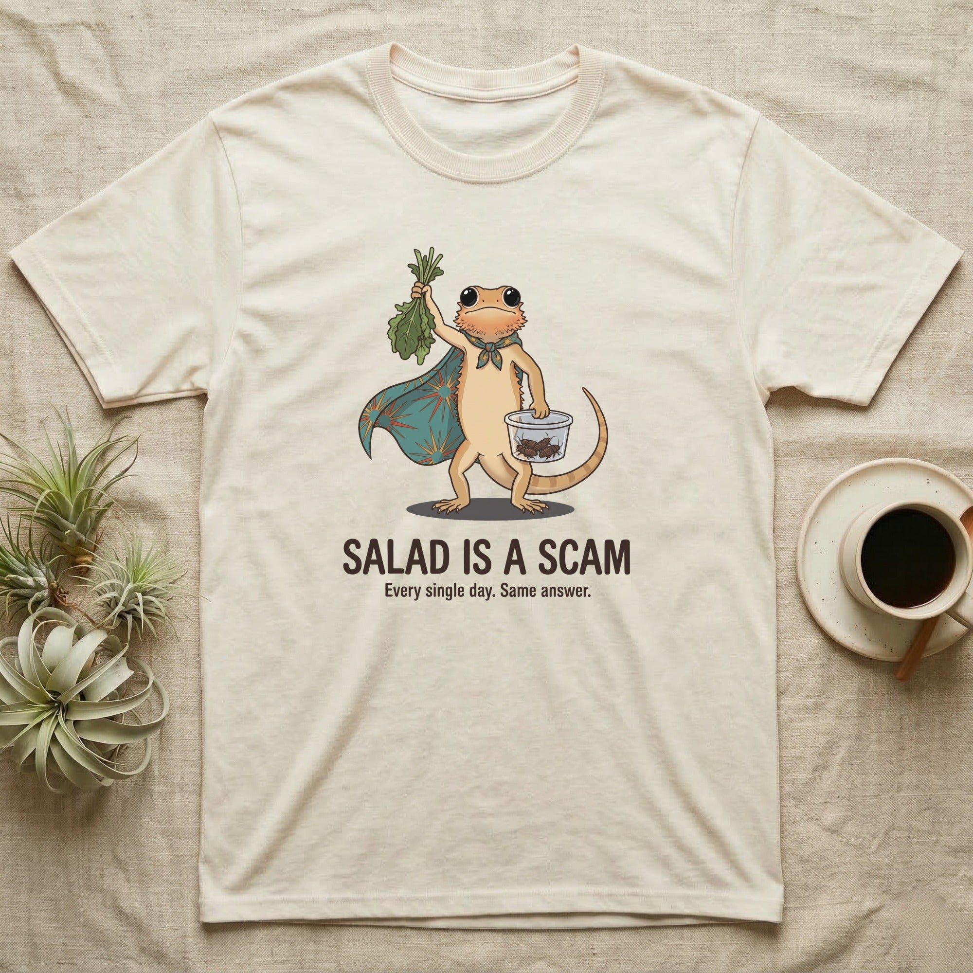 Bearded Dragon Salad Scam T-Shirt in Natural — Storybook-cartoon bearded dragon holding wilted greens at arm's length and a tub of roaches, captioned "Salad Is a Scam".