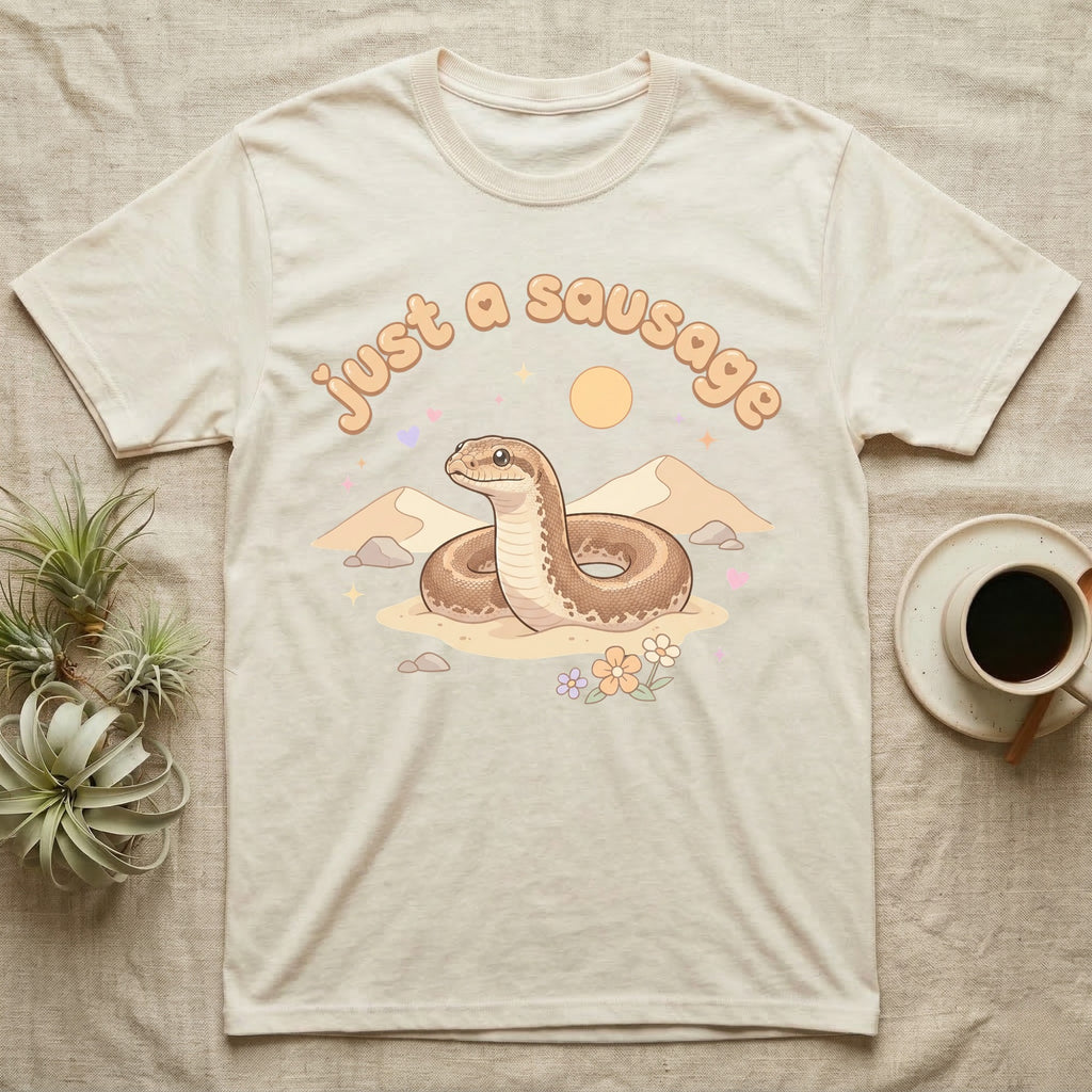 Kenyan Sand Boa Softie T-Shirt in Natural — Kenyan sand boa looping out of pastel sand dunes under a puffy "just a sausage" bubble wordmark with tiny hearts.