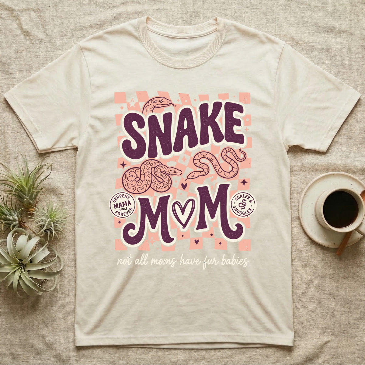 Cream t-shirt with "Snake Mom" design featuring snakes, hearts, and checkerboard pattern.
