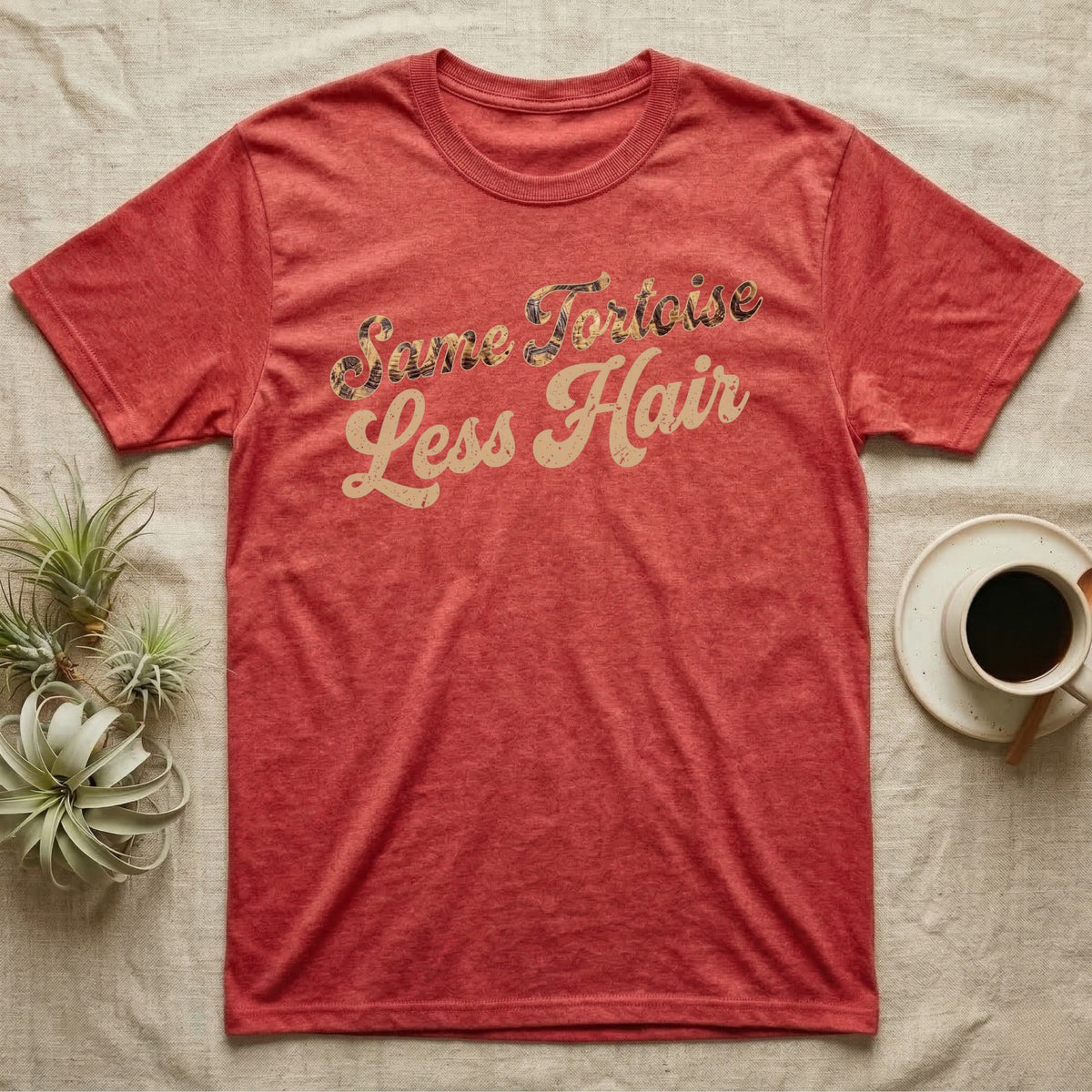 Tortoise Owner Retro T-Shirt in Heather Red — Worn 1970s brush script reading Same Tortoise in tortoise-shell texture over Less Hair in warm sand, climbing a diagonal on charcoal grey