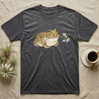 Pacman Frog Blossom T-Shirt in Dark Heather — Watercolor illustration of an olive-tan Pacman frog holding a water-lily blossom sprig, on a dark grey t-shirt.