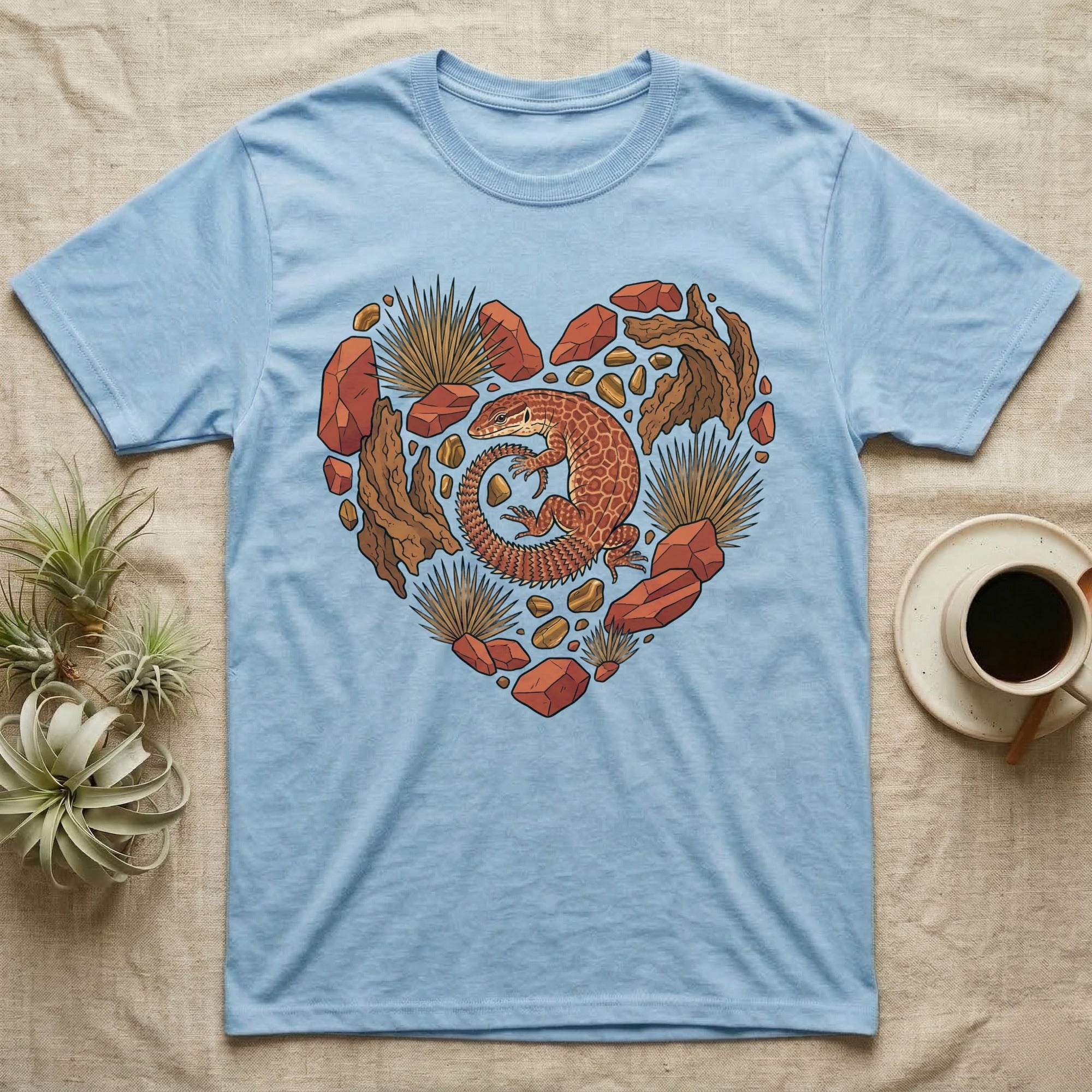 Blue t-shirt with a heart-shaped design of a lizard, rocks, and plants.