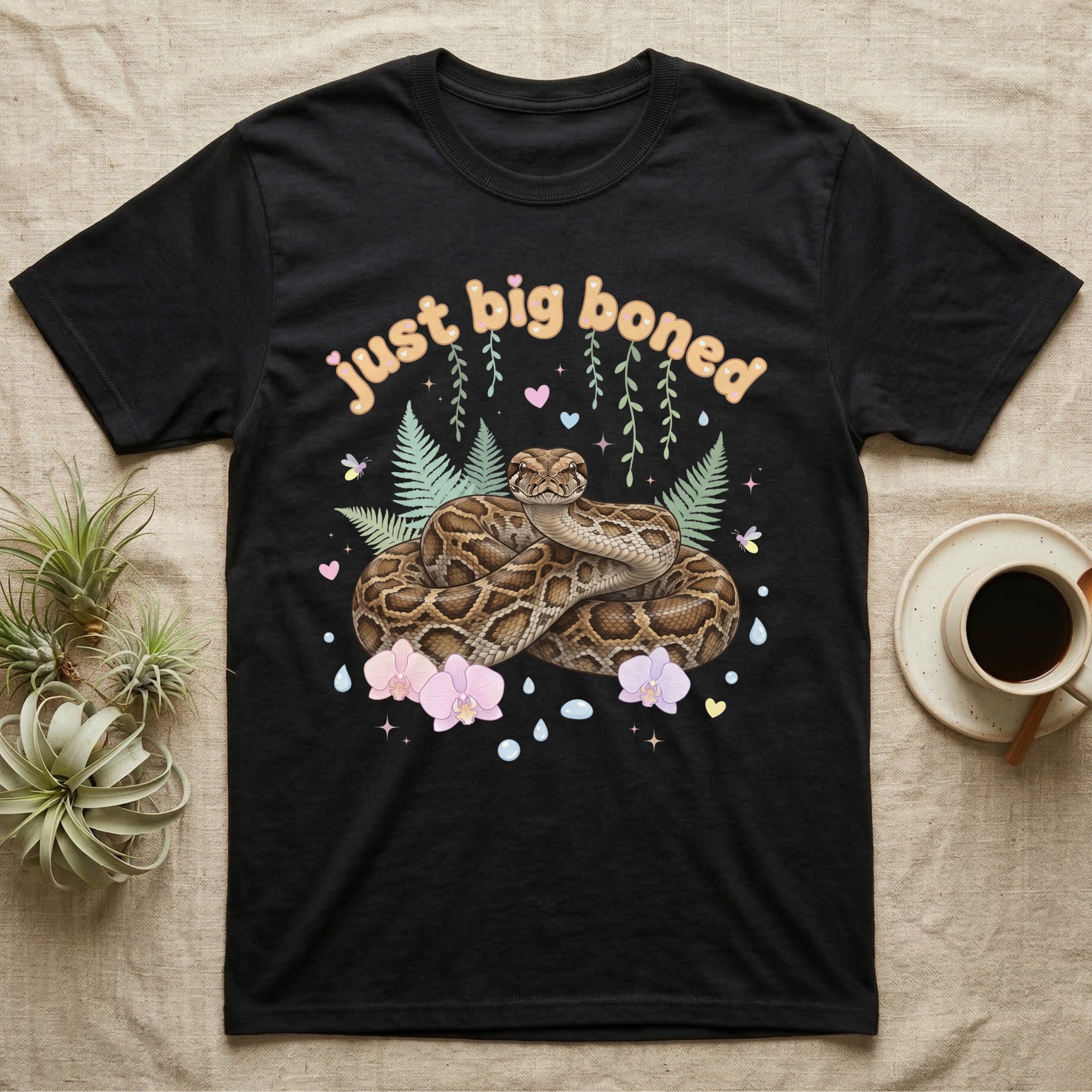 Burmese Python Baby T-Shirt in Black — Massive coiled Burmese python among pastel ferns and orchids under puffy butterscotch bubble text "just big boned".