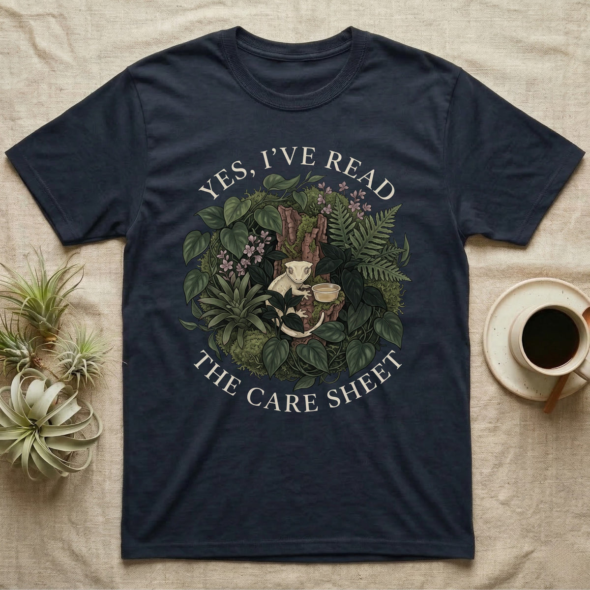 Crested Gecko Care Sheet T-Shirt in Navy — Botanical wreath of pothos and moss circling a crested gecko, closed by two arcs of Roman capitals.