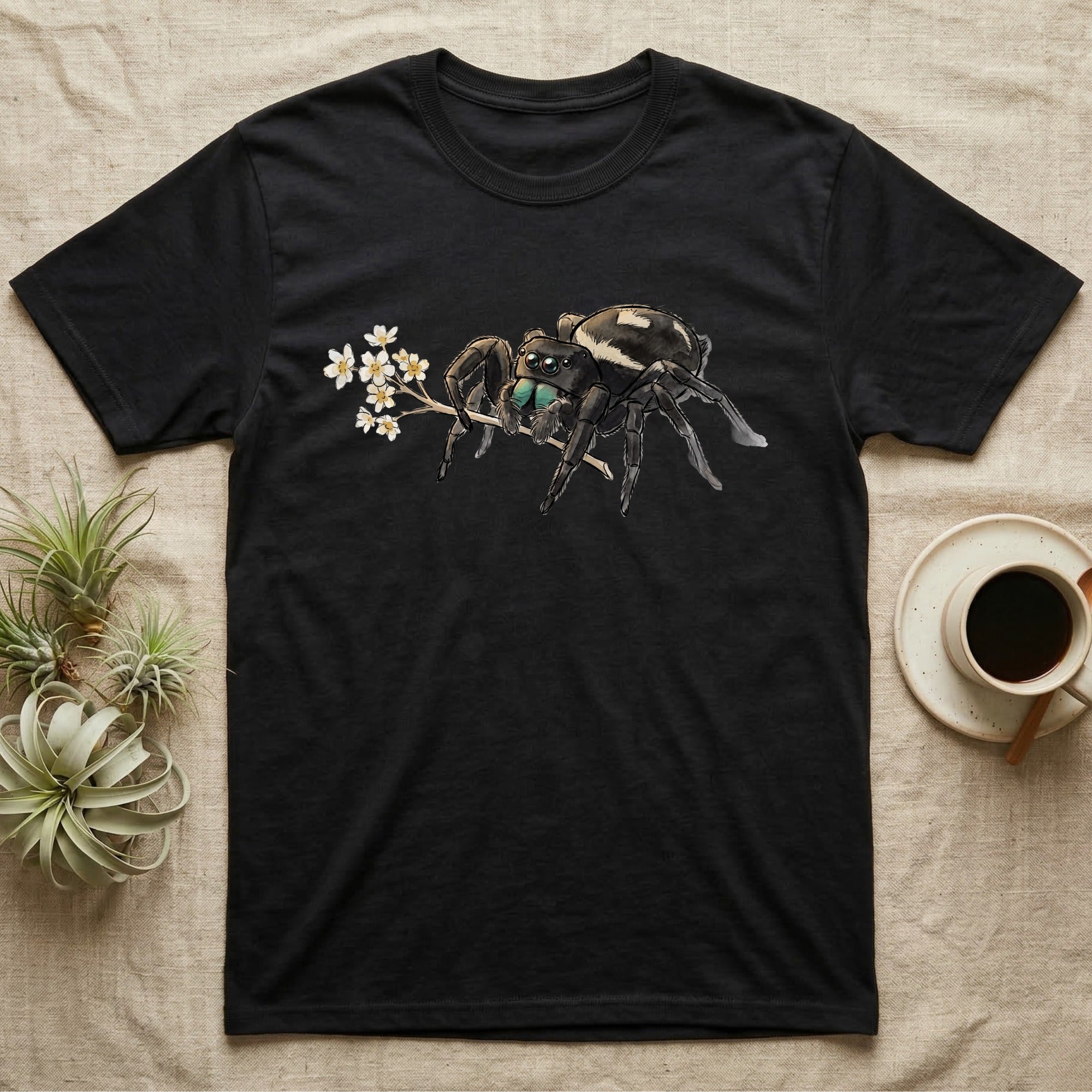 Jumping Spider Blossom T-Shirt in Black — Watercolor illustration of a black regal jumping spider with iridescent eyes holding a tiny wildflower sprig, on a dark grey t-shirt.