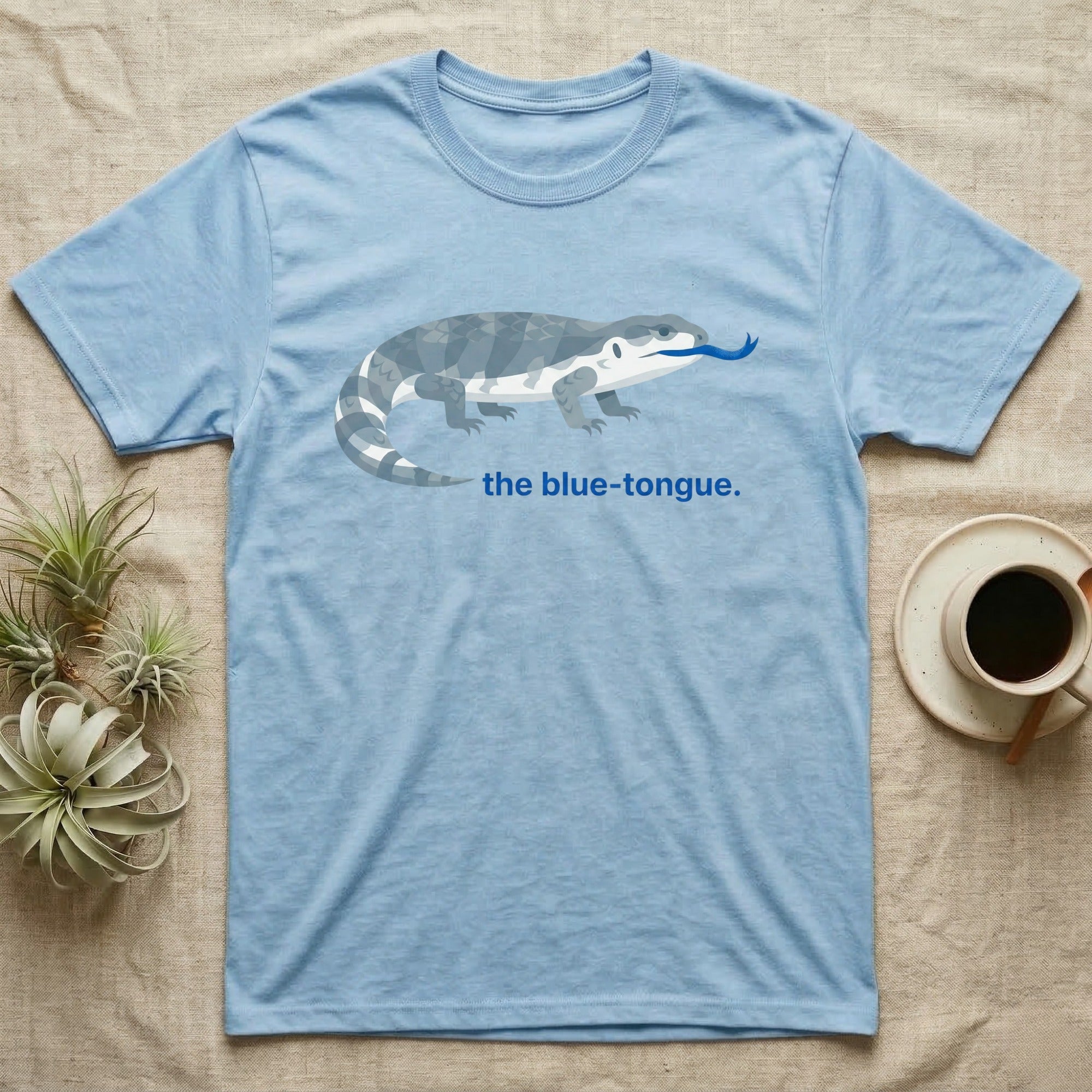Light blue t-shirt with a grey and blue patterned lizard and text "the blue-tongue."