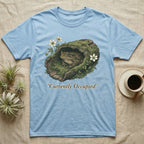 Light blue t-shirt with a toad in a mossy log with flowers, text "Currently Occupied".