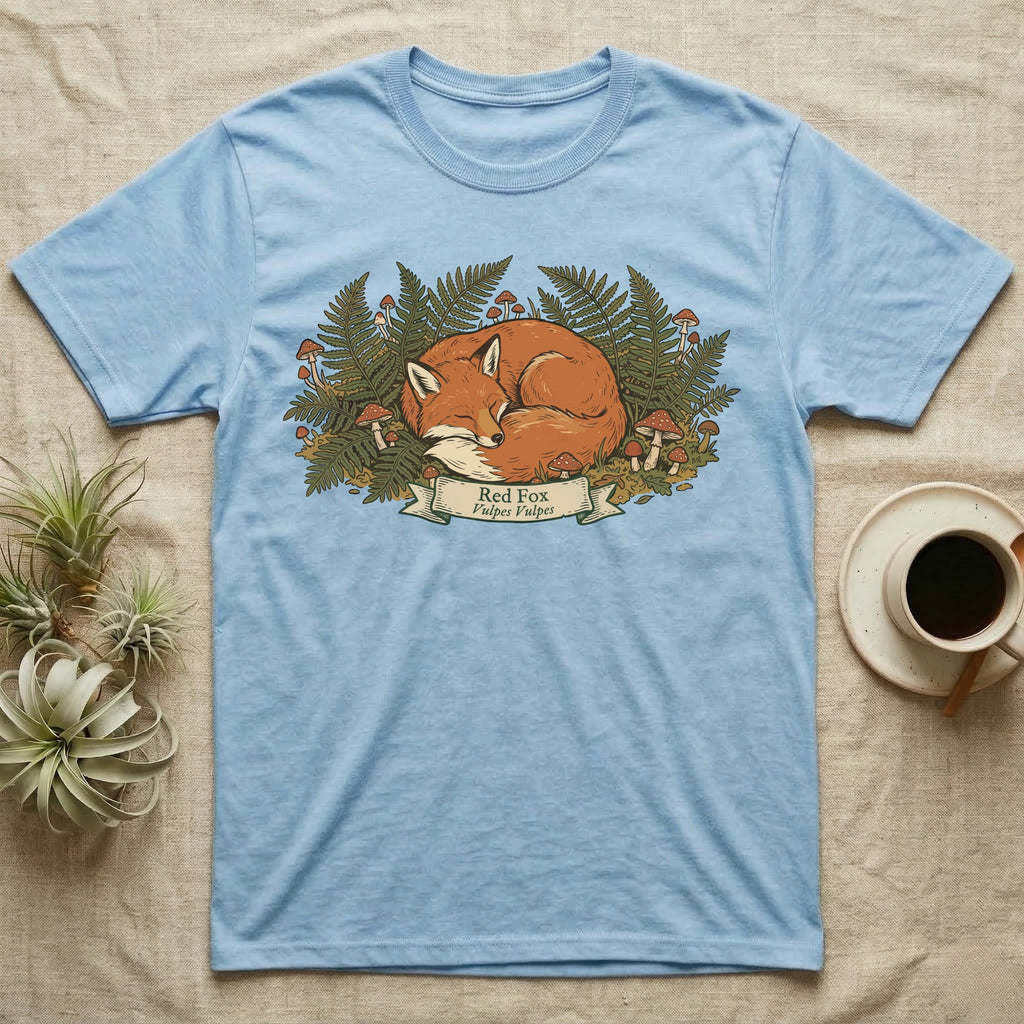 Blue t-shirt featuring a sleeping red fox surrounded by ferns and mushrooms.