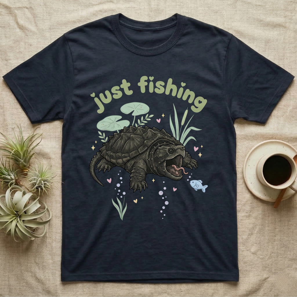 Alligator Snapping Turtle Softie T-Shirt in Navy — Alligator snapping turtle with open mouth and tongue lure under a puffy pastel "just fishing" bubble wordmark.