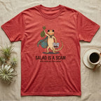 Bearded Dragon Salad Scam T-Shirt in Heather Red — Storybook-cartoon bearded dragon holding wilted greens at arm's length and a tub of roaches, captioned "Salad Is a Scam".