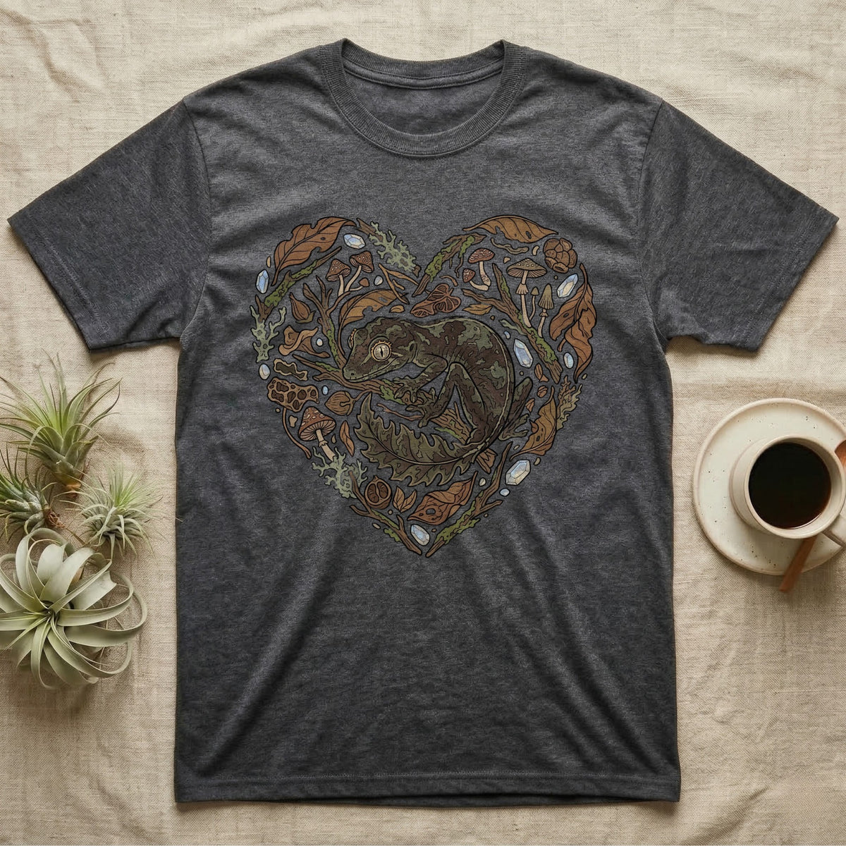Dark grey t-shirt with a heart-shaped design of a gecko surrounded by leaves and mushrooms.