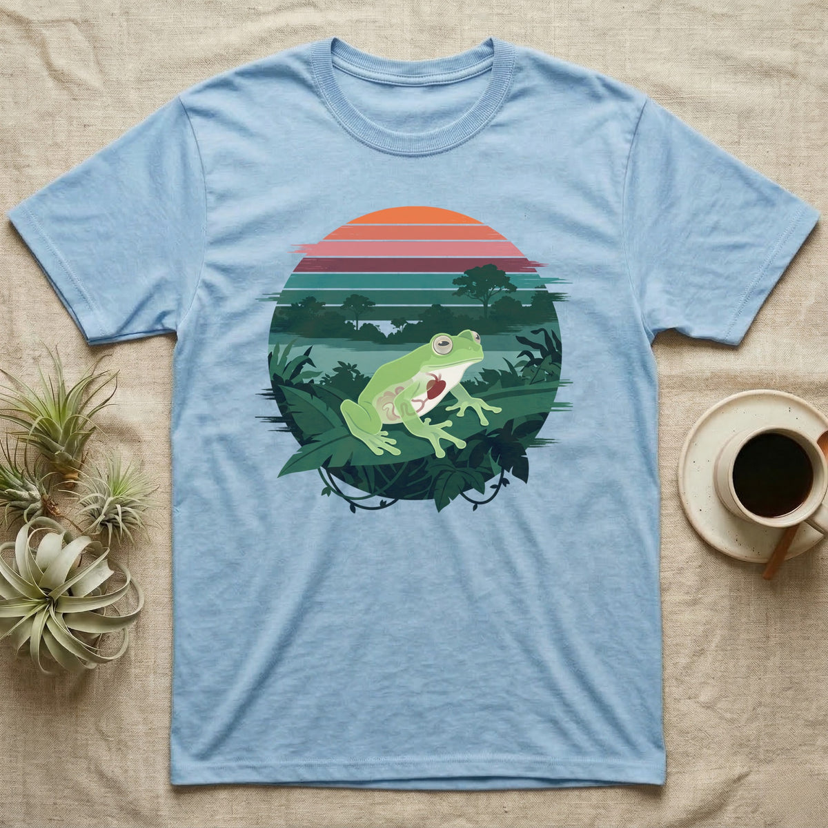 Glass Frog See-Through T-Shirt in Light Blue — Flat-colour circle-window illustration of a glass frog silhouetted crossing a rainforest canopy scene.