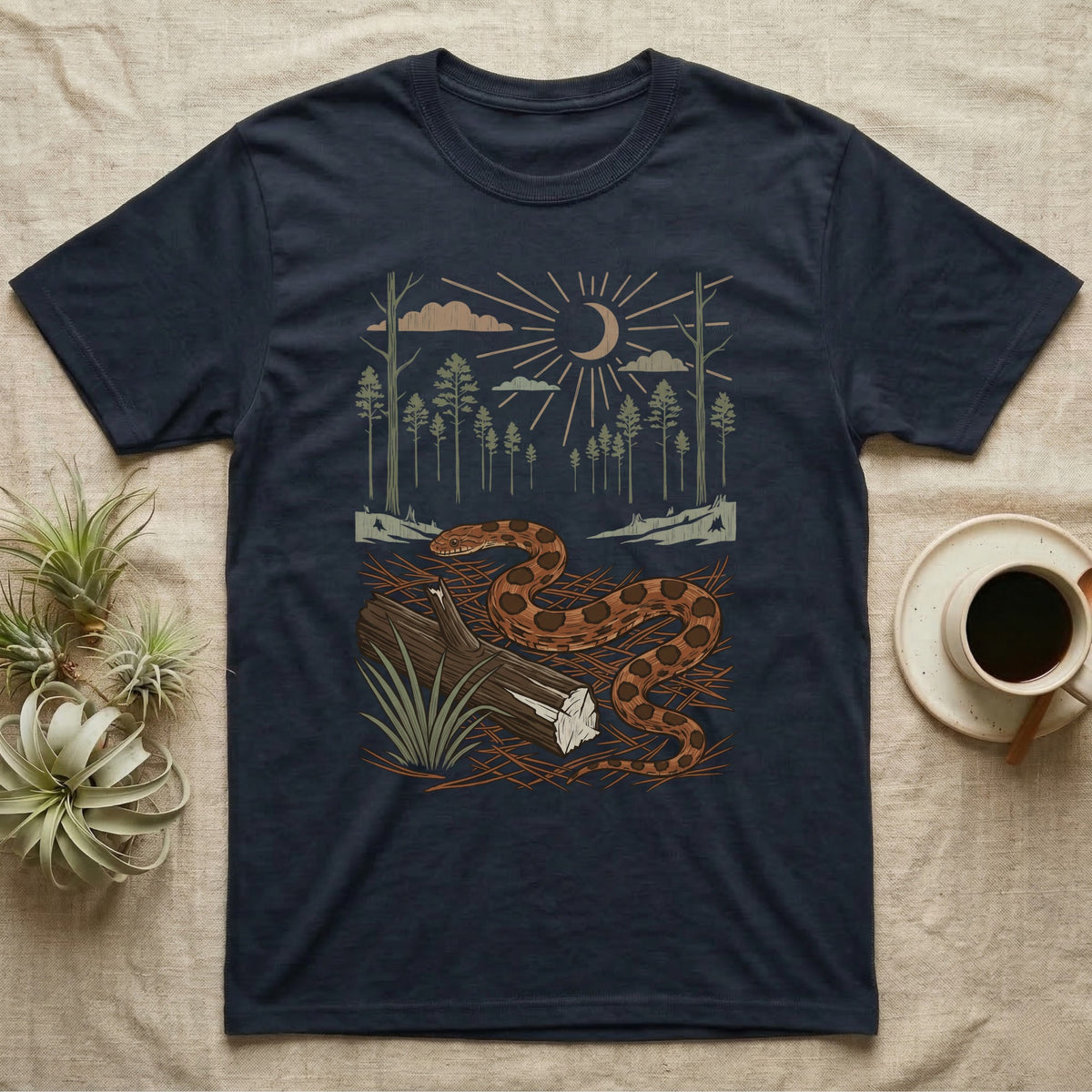 Corn Snake Home Range T-Shirt in Navy — Woodcut-style illustration of a corn snake winding across pine straw beside a split log with pine trees behind, no on-shirt text.