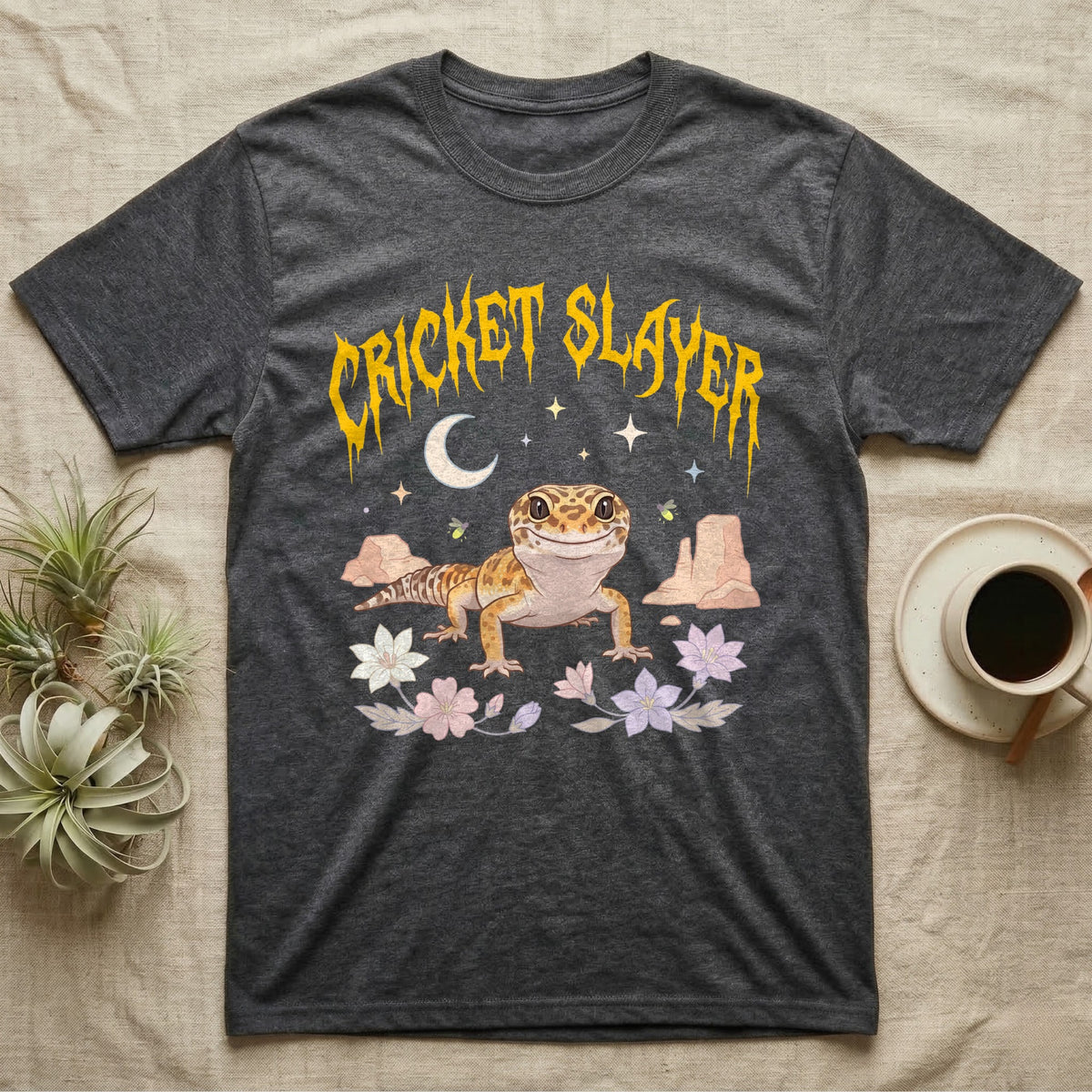 Leopard Gecko Feral T-Shirt in Dark Heather — Smiling leopard gecko in a pastel desert-night scene under a spiky golden metal wordmark reading CRICKET SLAYER.