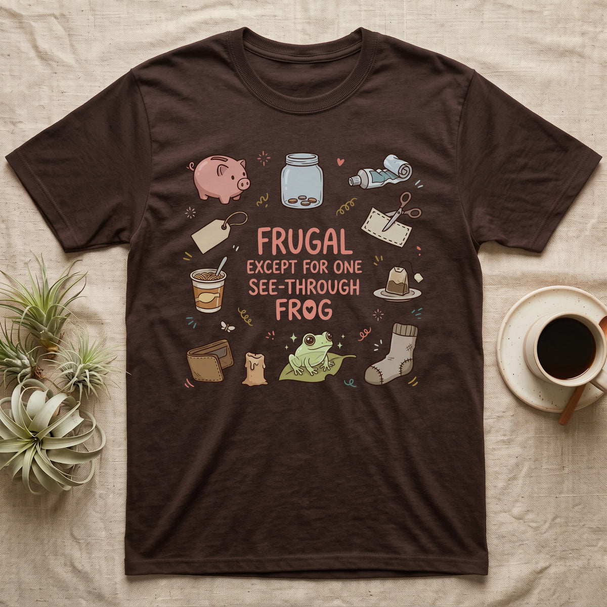 Glass Frog Frugal T-Shirt in Dark Chocolate — Cartoon glass frog on a leaf under the words Frugal except for one see-through frog, ringed by a piggy bank, coin jar, coupons and other thrifty things