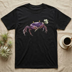 Vampire Crab Blossom T-Shirt in Black — Watercolor illustration of a violet-purple vampire crab with yellow eye stalks holding a moss-flower blossom sprig, on a dark grey t-shirt.