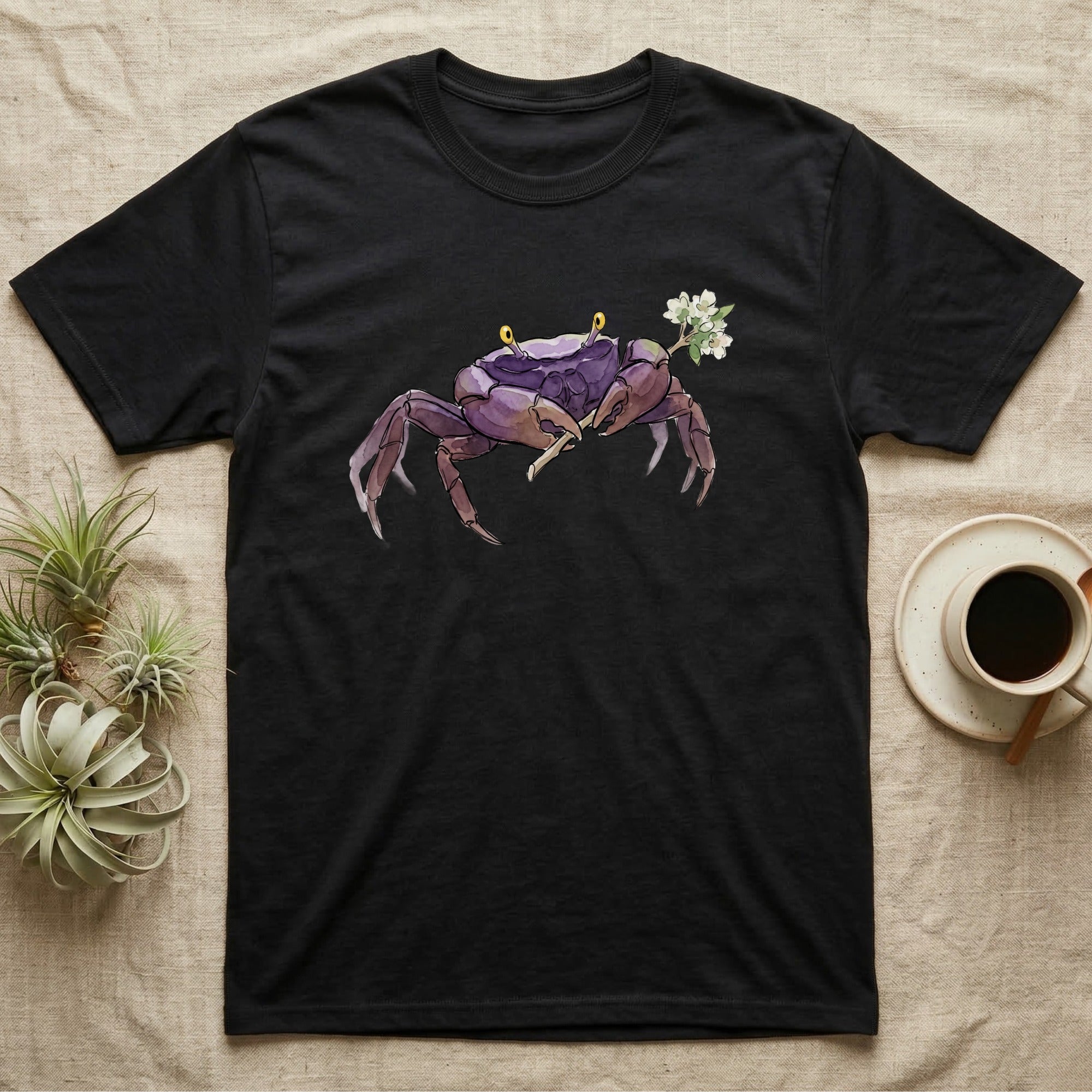 Vampire Crab Blossom T-Shirt in Black — Watercolor illustration of a violet-purple vampire crab with yellow eye stalks holding a moss-flower blossom sprig, on a dark grey t-shirt.