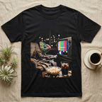 Veiled Chameleon TV Static T-Shirt in Black — Veiled chameleon slouched in an armchair with a remote, its head glowing in retro TV test-pattern colour bars.