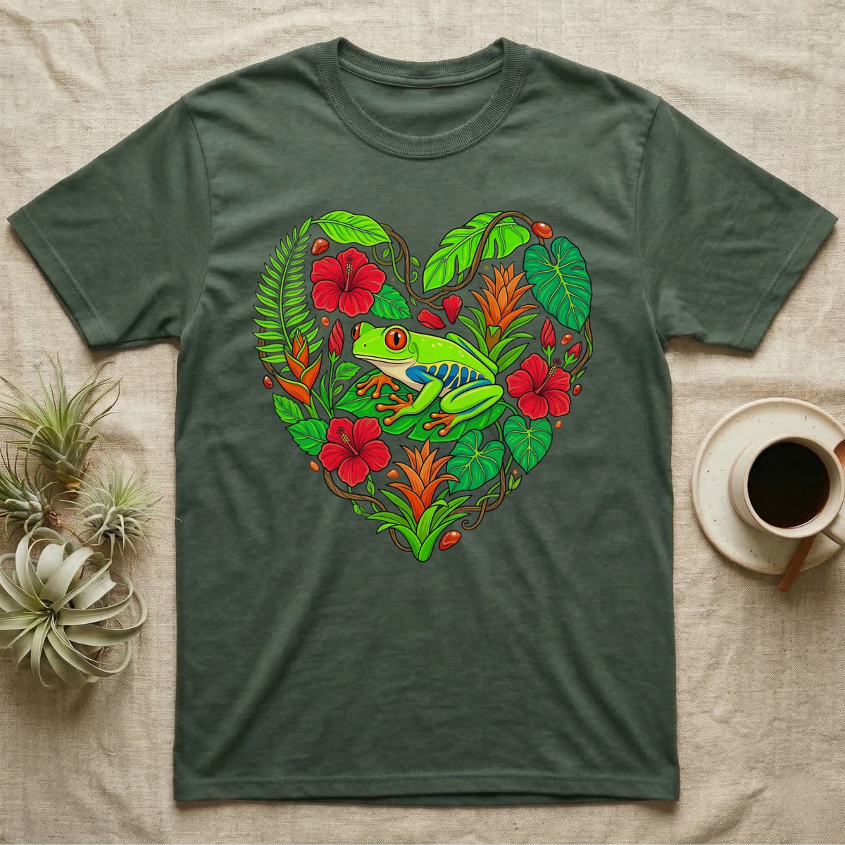 Green t-shirt with a heart-shaped design of a red-eyed tree frog among tropical leaves and flowers.