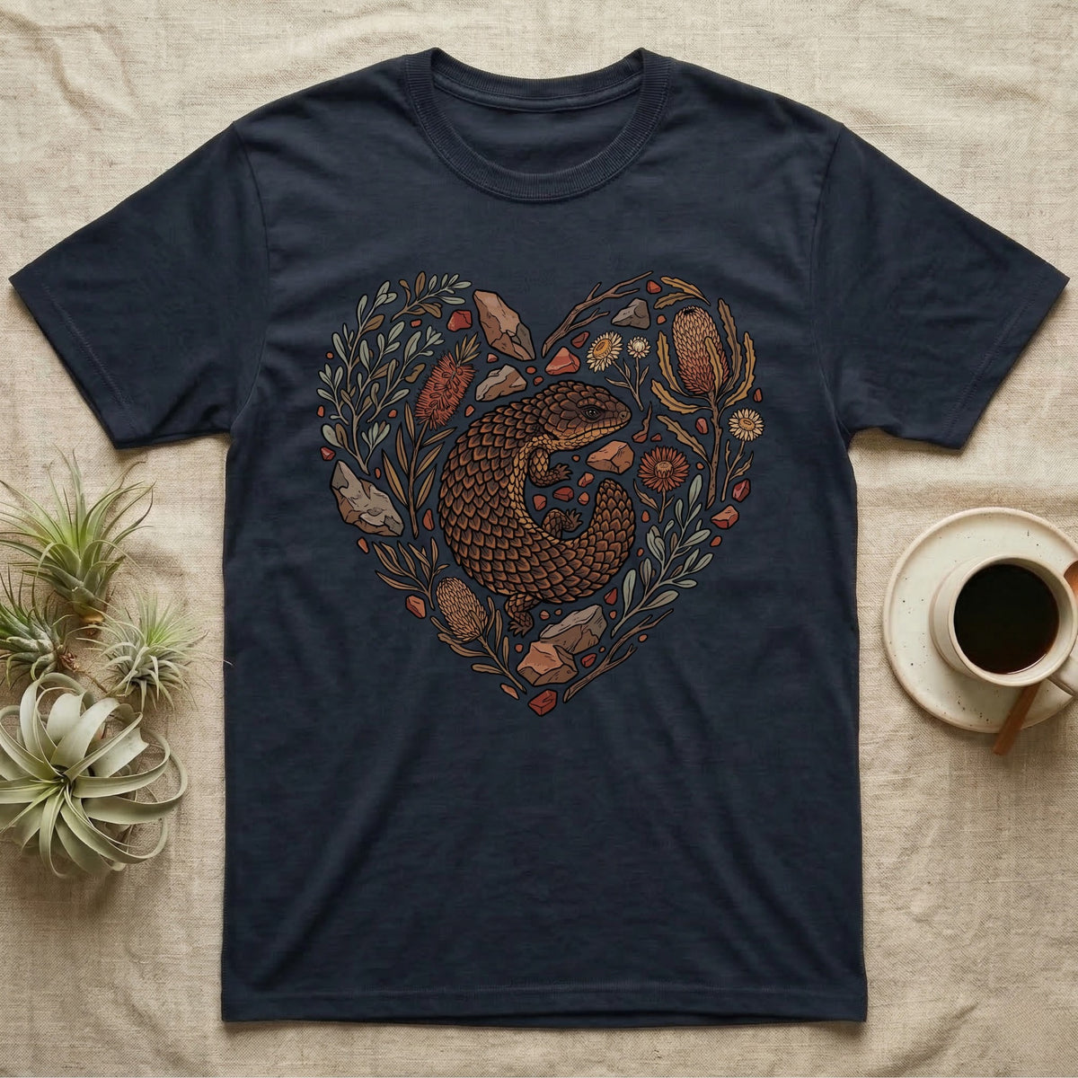 Dark t-shirt with a heart-shaped design featuring a lizard surrounded by flowers and stones.