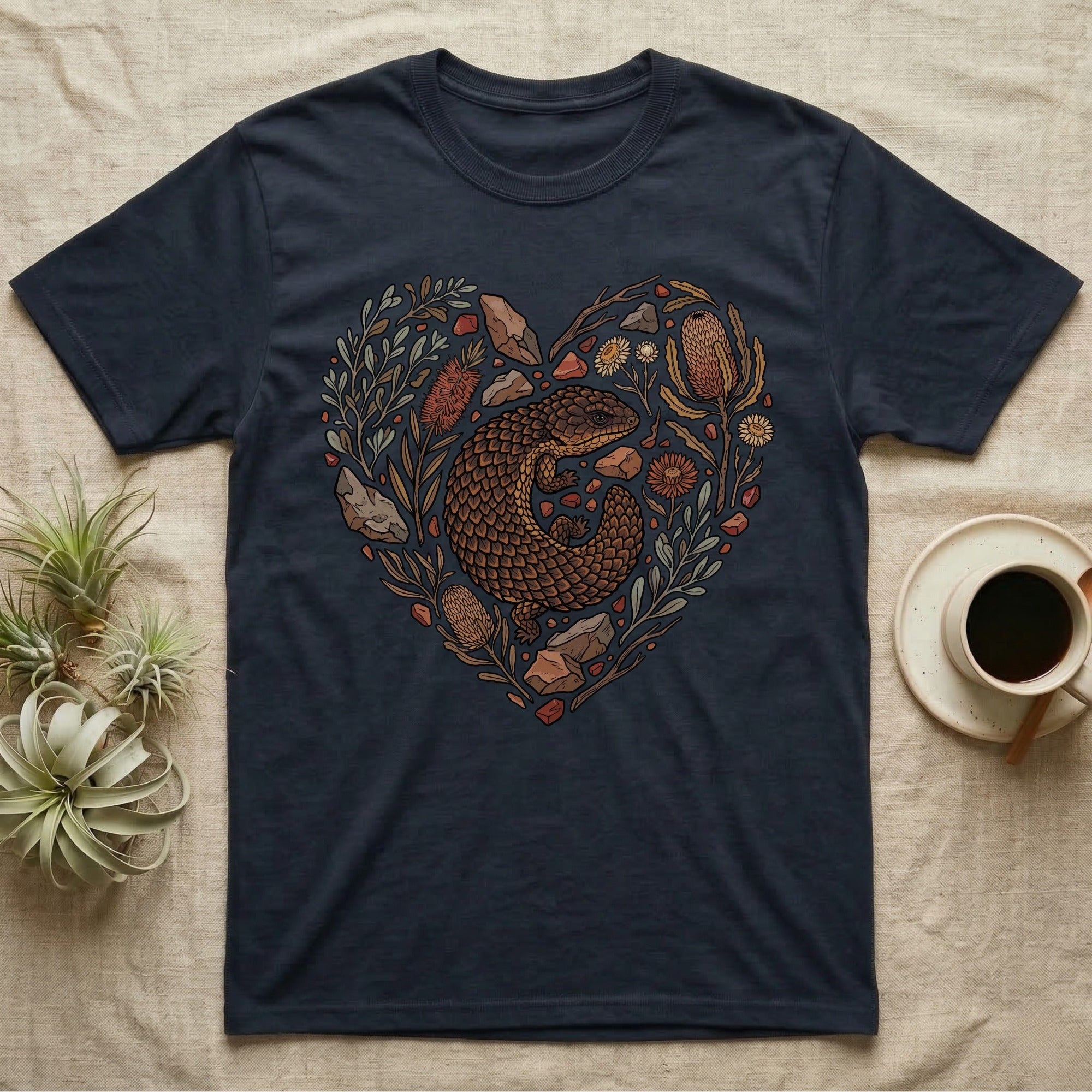 Dark t-shirt with a heart-shaped design featuring a lizard surrounded by flowers and stones.