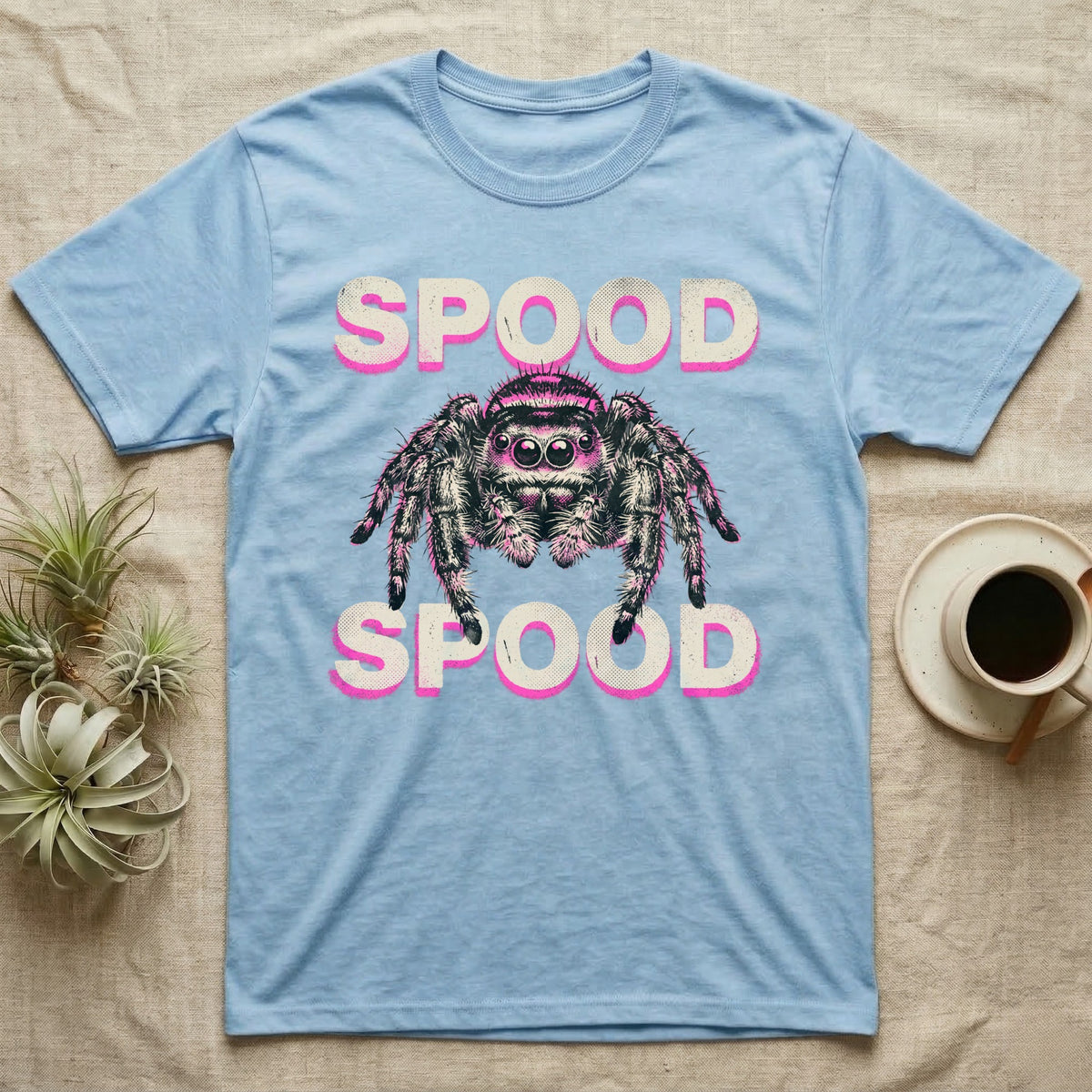 Spood Jumping Spider T-Shirt in Light Blue — Grunge-punk illustration of an oversized front-facing jumping spider with a distressed "Spood" wordmark in bone and acid pink.