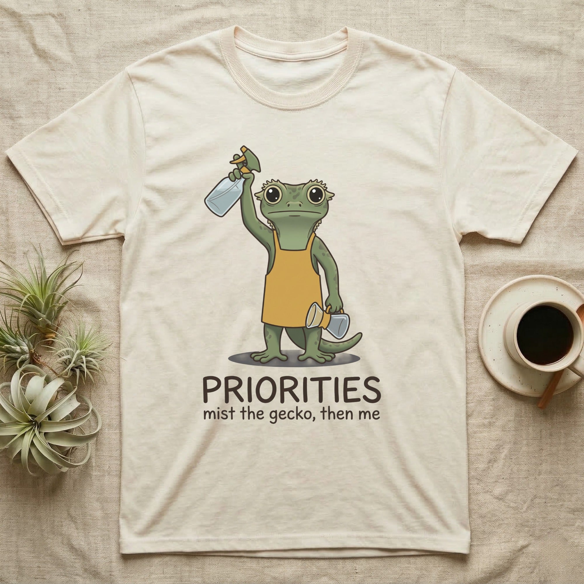 Crested Gecko Coffee T-Shirt in Natural — Storybook crested gecko standing with a raised spray mister and a pour-over coffee, text priorities below