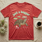 Red-Eared Slider Softie T-Shirt in Heather Red — Red-eared slider turtle stretching its neck to beg, under pastel bubble text "just a beggar" with hearts.