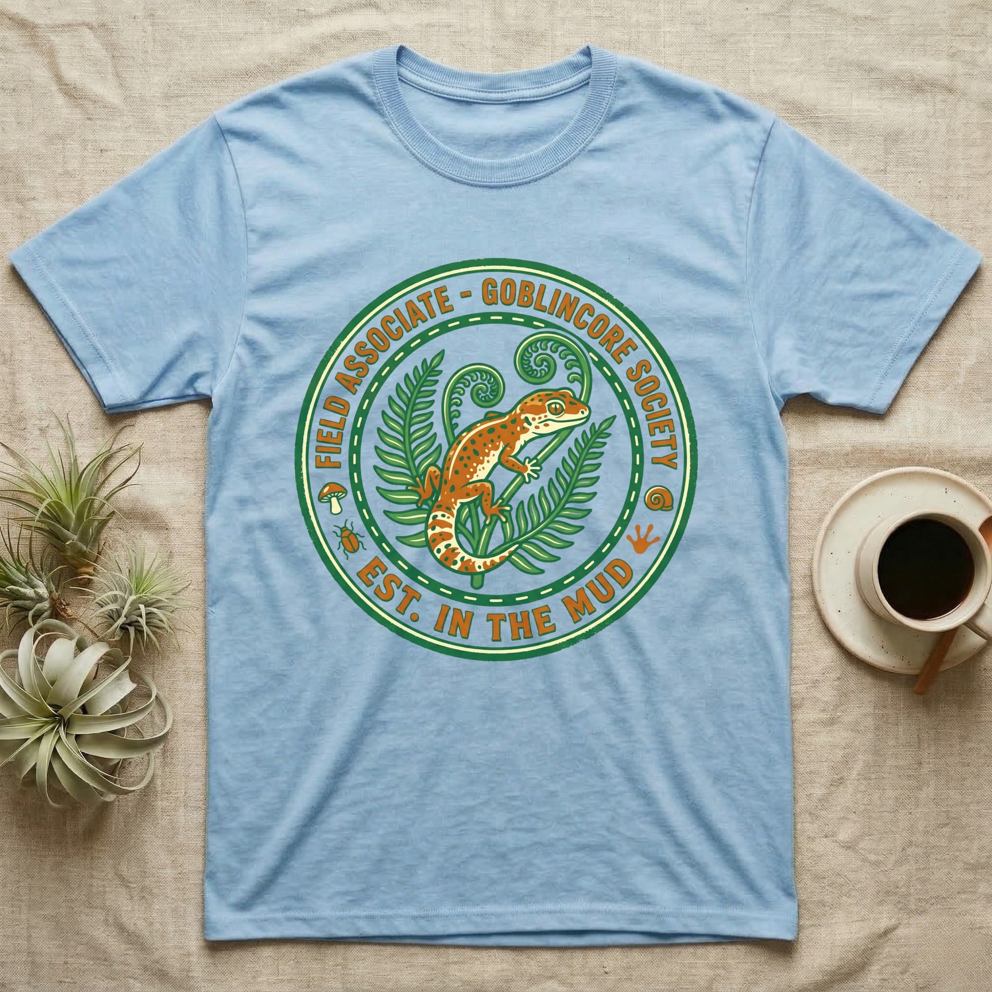 Light blue t-shirt with circular "Goblincore Society" design featuring a gecko and ferns.