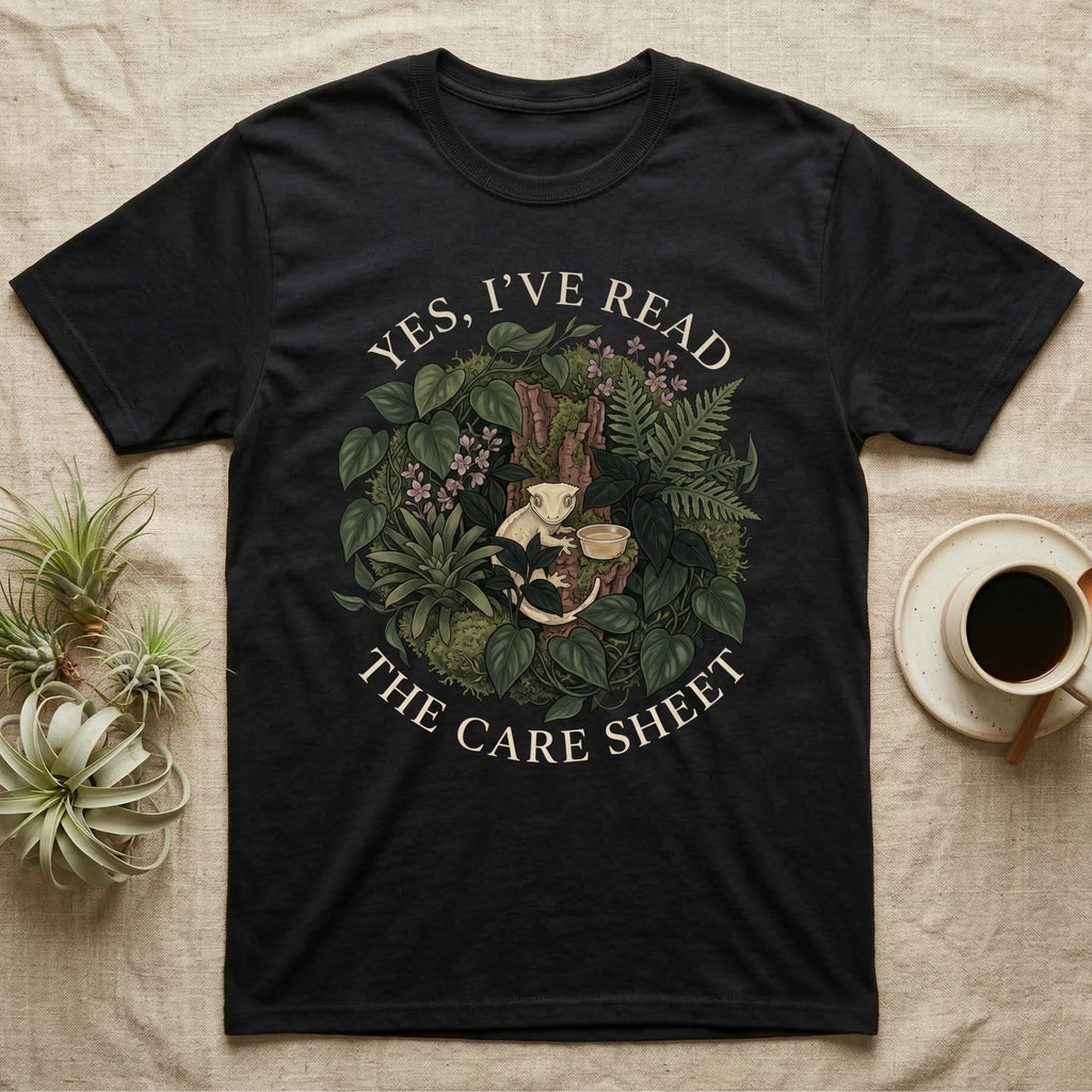 Crested Gecko Care Sheet T-Shirt in Black — Botanical wreath of pothos and moss circling a crested gecko, closed by two arcs of Roman capitals.