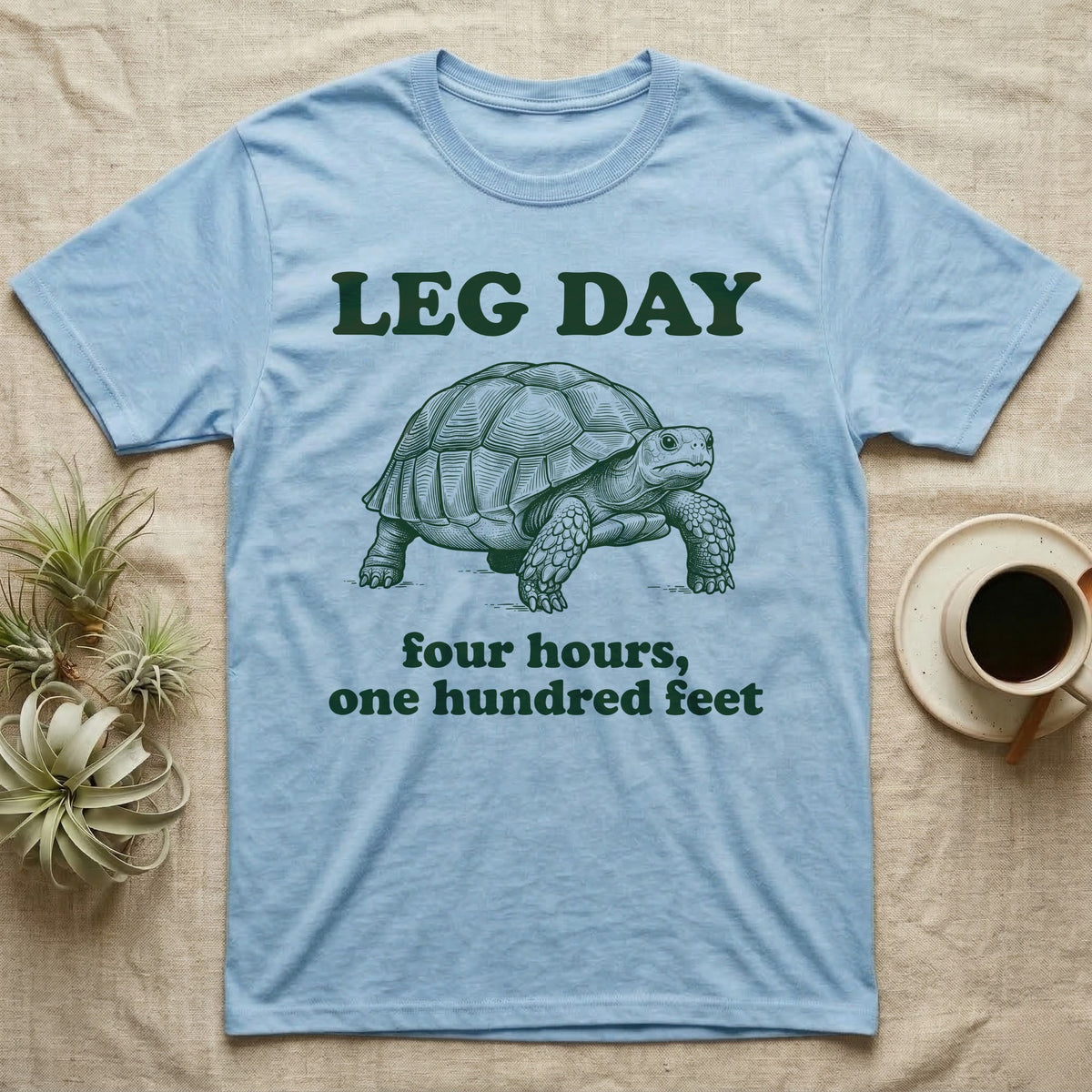 Sulcata Tortoise Leg Day T-Shirt in Light Blue — Engraved sulcata tortoise in deep green ink beneath the words LEG DAY, with four hours, one hundred feet below.