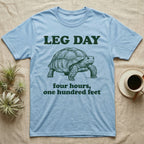 Sulcata Tortoise Leg Day T-Shirt in Light Blue — Engraved sulcata tortoise in deep green ink beneath the words LEG DAY, with four hours, one hundred feet below.
