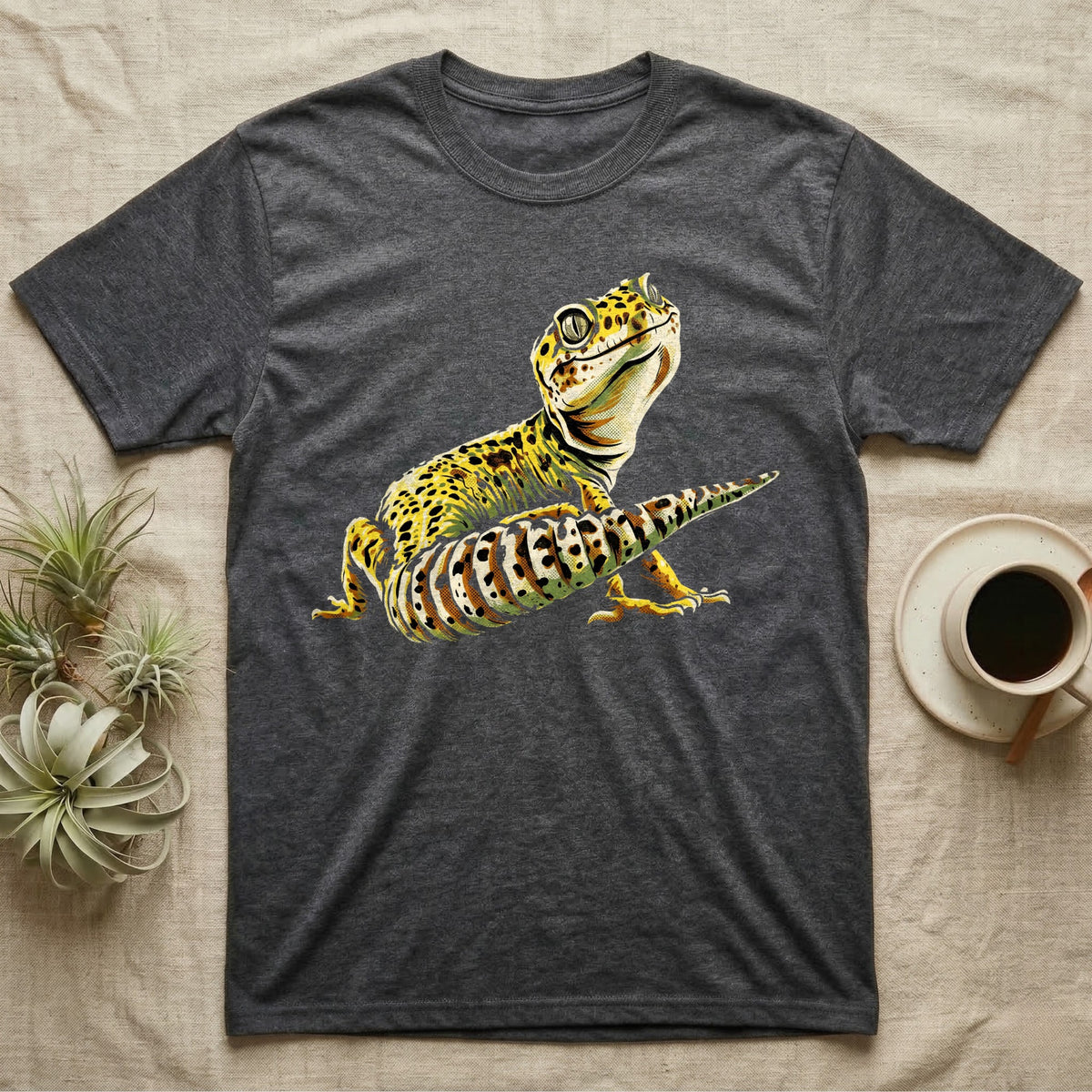 Illustration of a smiling leopard gecko with a plump curled spotted tail, bold vintage-comic ink outlines and halftone shading, graphic-only, no text. — shown on a Dark Heather tee.