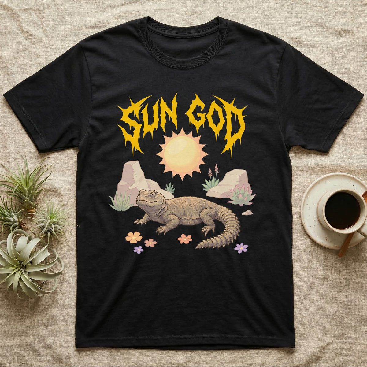 Moroccan Uromastyx Feral T-Shirt in Black — Moroccan uromastyx basking under a big sun with a jagged solar-gold metal "SUN GOD" wordmark and pastel desert scene.