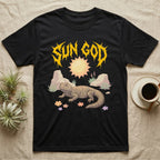 Moroccan Uromastyx Feral T-Shirt in Black — Moroccan uromastyx basking under a big sun with a jagged solar-gold metal "SUN GOD" wordmark and pastel desert scene.