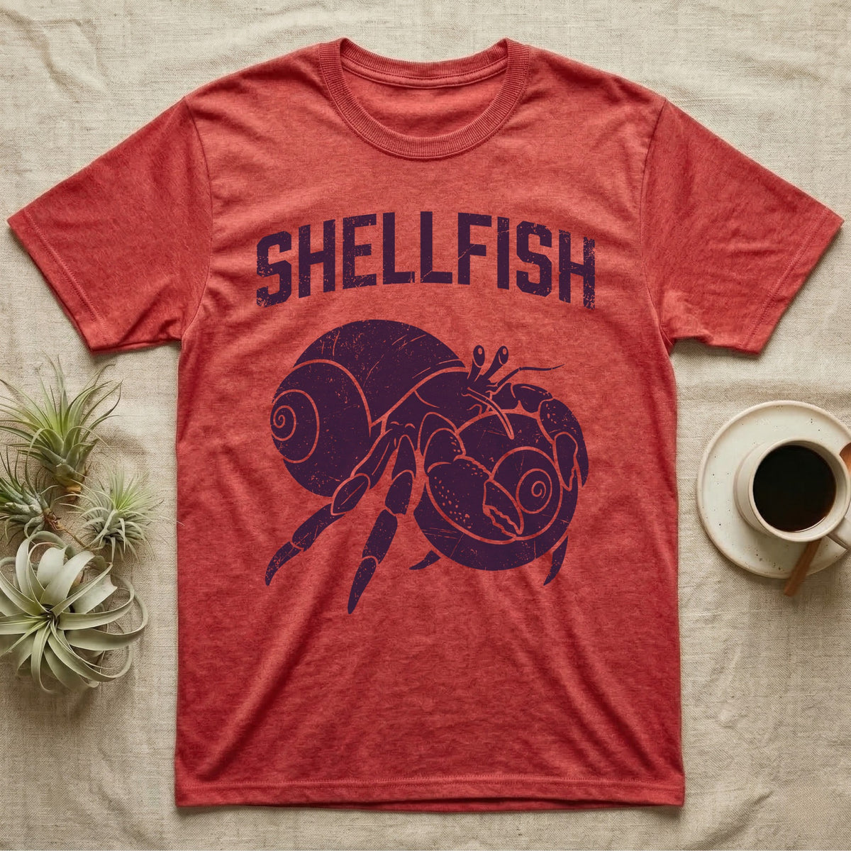 Hermit Crab Shellfish T-Shirt in Heather Red — Worn purple one-ink print of a hermit crab hugging a big spare shell to its chest under the word Shellfish
